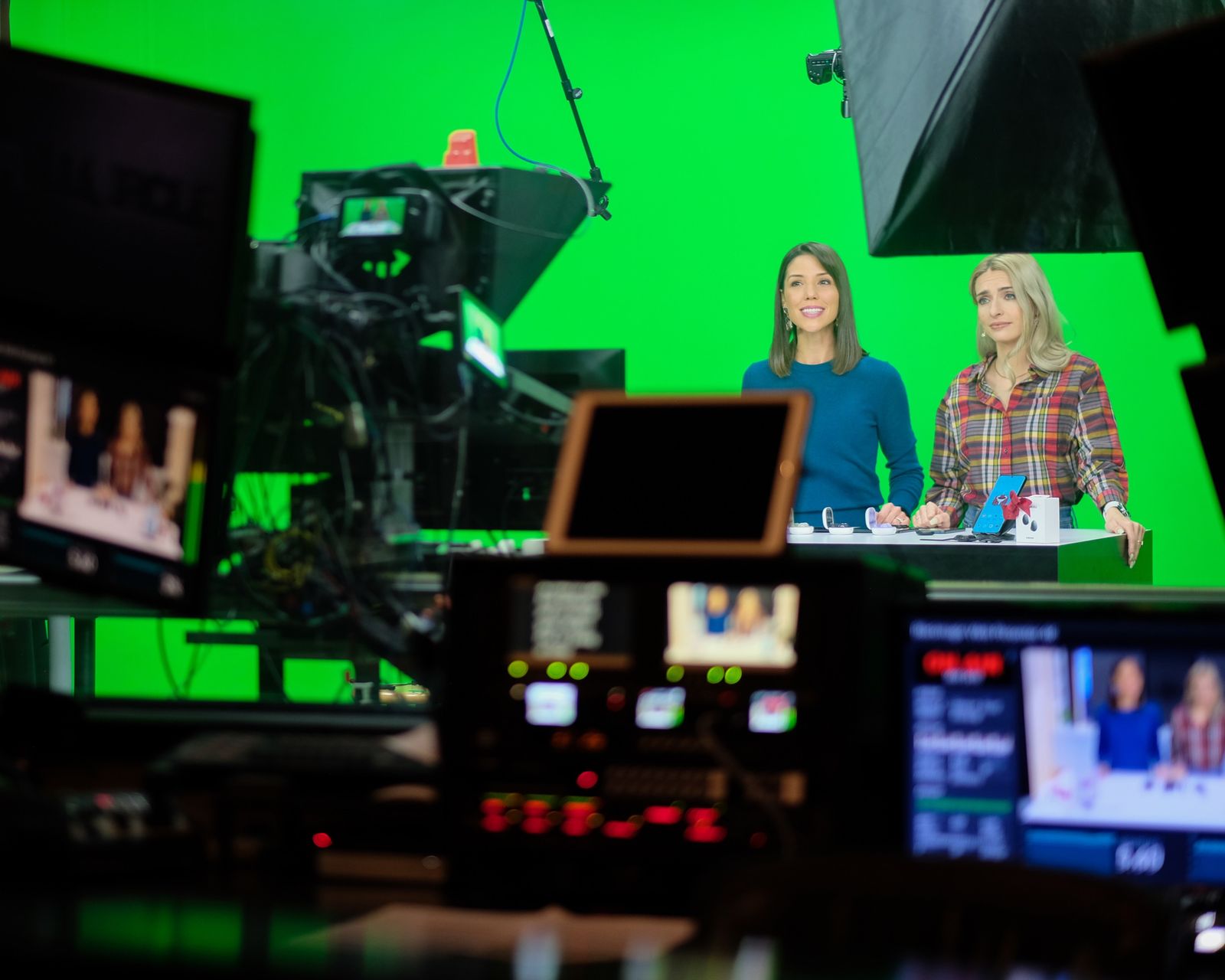 Two hosts on the green screen set with camera monitors in the foreground